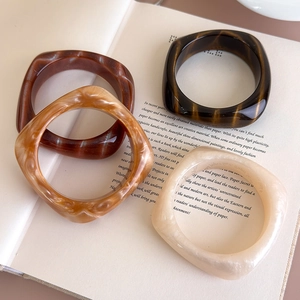 Dettaglio di bracciali quadrati in acrilico con motivi marmorizzati e tartarugati su un libro