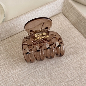 Dettaglio del fermaglio per capelli in resina marrone caffè con scritta dorata decorativa