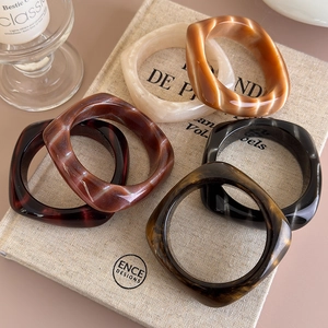 Dettaglio di bracciali quadrati in acrilico con trama marmorizzata in vari colori caldi