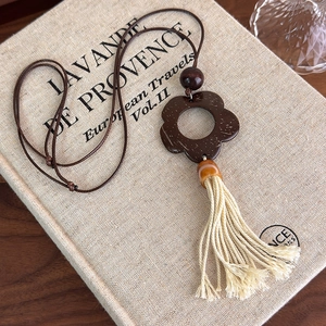 Detailed shot of vintage wood flower pendant with cotton tassel on a textured linen background
