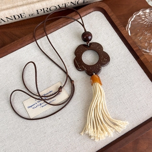Detail view of vintage coconut shell flower pendant with long off-white tassel on a sweater chain