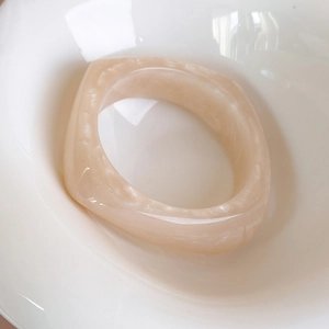 Primo piano di un ampio bracciale quadrato in acrilico con venature marmoree beige su ceramica