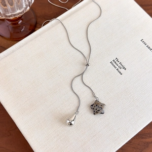 Detailed close-up of a silver Y-chain necklace featuring a spotted stone star and metal droplet