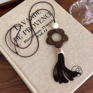 Detailed macro view of hollowed floral pendant with dark brown tassel and woven cord