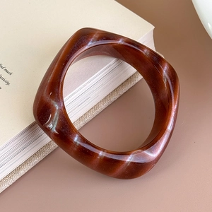Dettaglio di un bracciale quadrato in acrilico ambra con trama marmorea perlata su libro