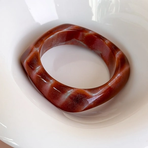 Dettaglio macro di un bracciale quadrato in resina acrilica marrone-rossastra marmorizzata