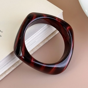 Dettaglio del bracciale quadrato in acrilico marrone marmorizzato appoggiato a un libro bianco