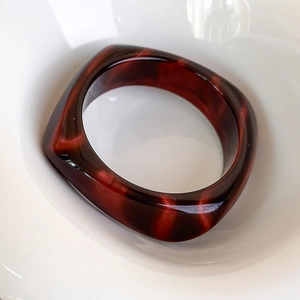 Macro di un ampio bracciale in acrilico con motivo marmorizzato in una ciotola di ceramica