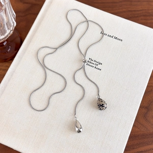 Detail of silver adjustable snake chain with teardrop stone pendant and polished metal charm