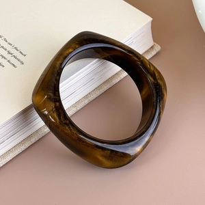 Dettaglio di un bracciale rigido quadrato in resina con motivo ambrato e finitura lucida