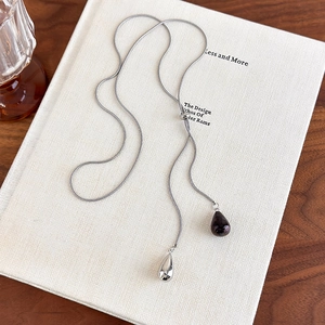 Detail of silver snake chain necklace with teardrop pendants on a book