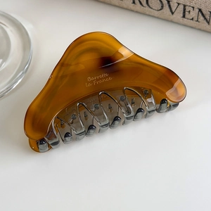 Detail of amber acetate hair claw clip with French lettering on white minimalist surface