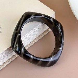 Dettaglio del bracciale quadrato in acrilico tartarugato su decorazione di libri minimalisti