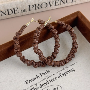 Détail de boucles d'oreilles créoles en cuir plissé marron avec fermoir doré
