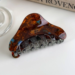 Detailed shot of amber and blue marbled acetate hair claw clip with gold lettering logo