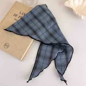 Detailed view of blue plaid cotton bandana with black wavy edges over vintage books