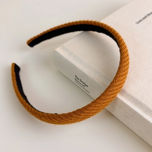 Dettaglio di cerchietto in maglia caramello con trama diagonale su sfondo di libro