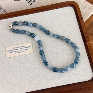 Macro detail of faceted blue natural stone beads with silver clasp on white fabric
