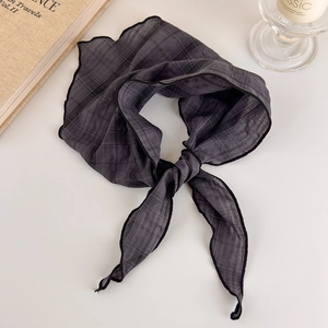 Detail of grey checkered headscarf featuring black wavy edges on a minimalist table