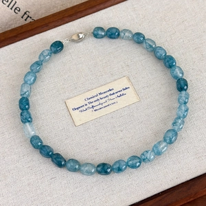 Detailed close-up of blue natural stone beaded necklace with a silver oval clasp on linen