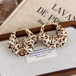 Detail of leopard print fabric hoop earrings on dark wood tray with rustic texture