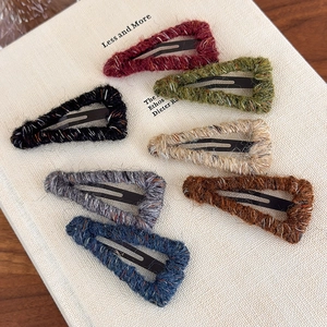 Knitted wool triangle hair clips in seven colors on a textured vintage book background