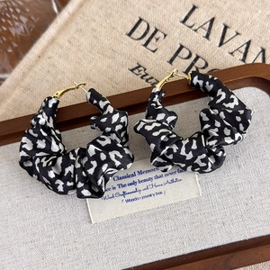 Detail of leopard print fabric wrapped hoop earrings with elegant gold hooks on linen