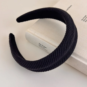 Detail view of a black wide ribbed knit headband displayed on a white book surface