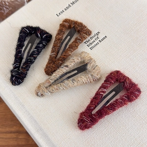 Detailed macro view of four wool-wrapped triangle hair clips in fall and winter colors