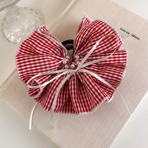 Close-up of red gingham bow hair claw with pearl accents on a vintage book surface