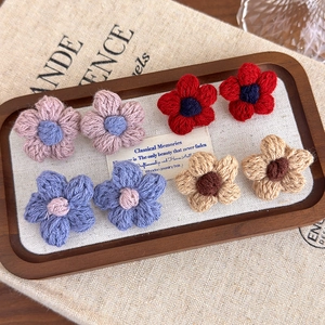 Detail of handmade knit flower earrings in four colors on a rustic wooden tray