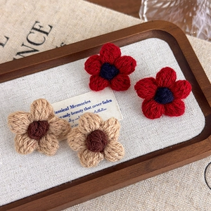Close-up of handmade crochet flower earrings in red and beige with detailed knit texture