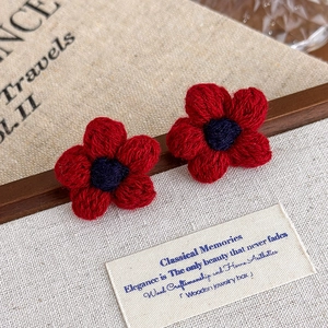 Detail of red handmade crochet flower earrings on a textured linen background