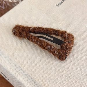 Macro shot of brown wool knitted drop-shaped hair clip on a minimalist linen book cover