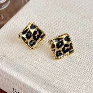 Detail of square leopard print earrings with gold metal frame on a white book surface