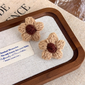 Close-up of handmade crochet flower earrings in brown and khaki on a wooden tray