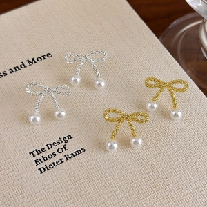 Elegant bow-shaped pearl stud earrings in gold and silver finish on a book background