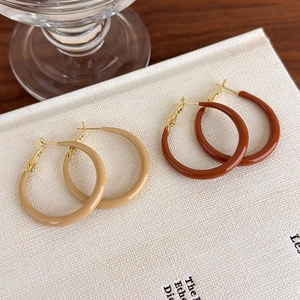 Close-up of caramel and beige enamel C-shaped hoop earrings with gold posts on book
