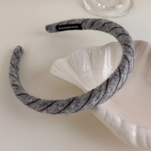 Detail of grey knitted headband featuring diagonal stripes and a handmade label