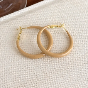 Close-up of beige glazed hoop earrings with golden metal clasps on textured background