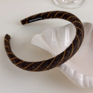 Detail of handmade knit headband with brown and yellow stripes on a white ceramic plate