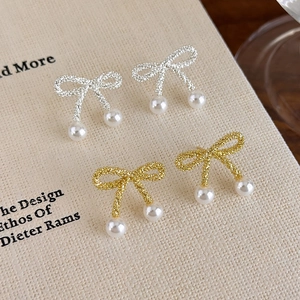 Detailed close-up of gold and silver bow pearl earrings with a stardust frosted texture