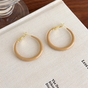 Detailed view of caramel enamel hoop earrings on a minimalist white book cover