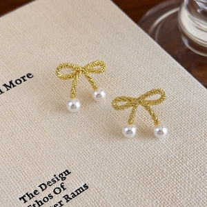 Close-up of golden bow-shaped stud earrings with pearls on a textured background