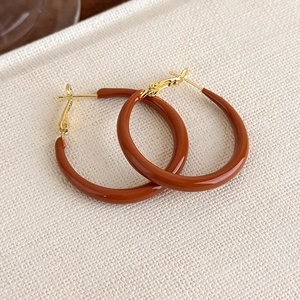 Macro shot of C-shaped caramel enamel hoop earrings with gold-tone metal studs