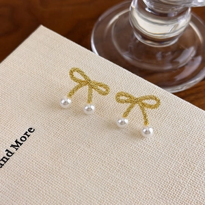 Detail of golden frosted bow earrings with miniature white pearls on a display card