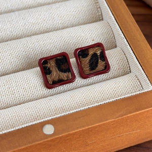 Gros plan de boucles d'oreilles carrées léopard avec cadre laqué bordeaux dans un écrin