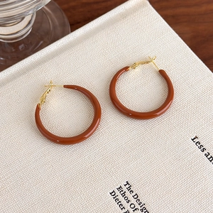 Macro shot of large caramel enamel C-shaped hoop earrings on a textured book surface