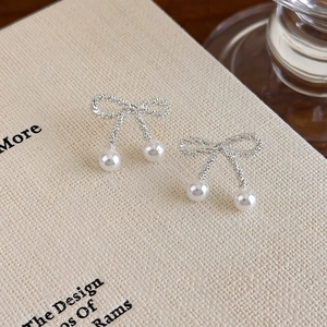 Detailed macro shot of elegant silver bow stud earrings with white pearl pendants