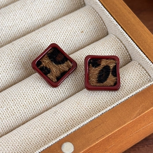 Détail de boucles d'oreilles carrées léopard avec bordure rouge sur plateau à bijoux